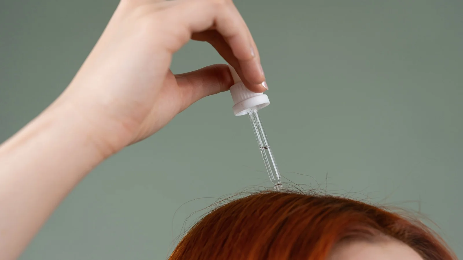 Soro de cabelo sendo aplicado cuidadosamente em um couro cabeludo visível.
